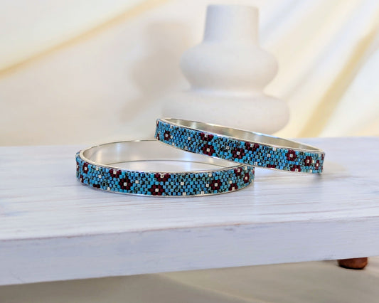 Two silver bangles with blue and red pattern on a white surface